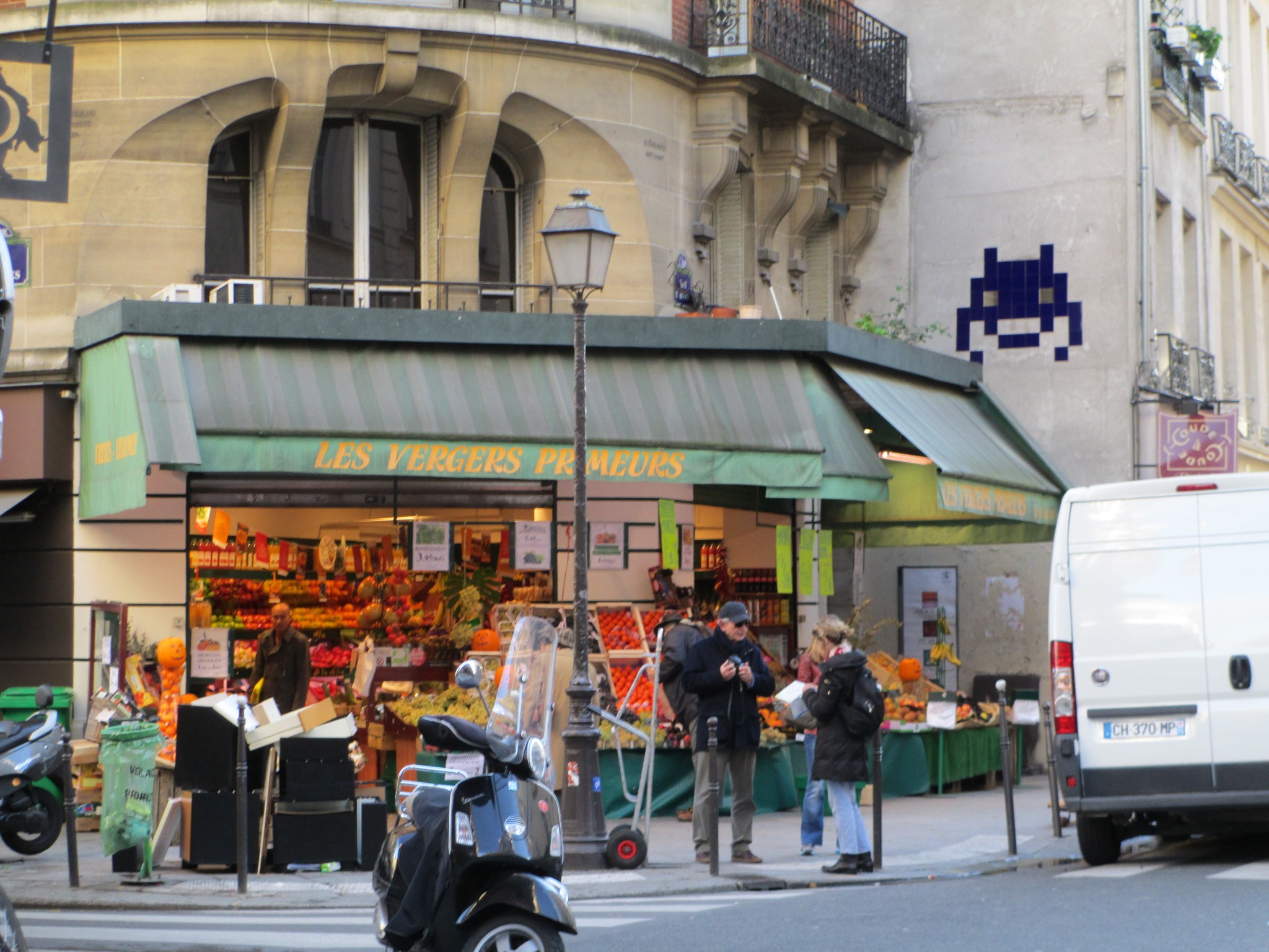Blue space invader mosaic above a green grocers on the corner of a street